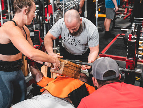 coach behind lifter as he squatsguy squatting with guys watching is every move