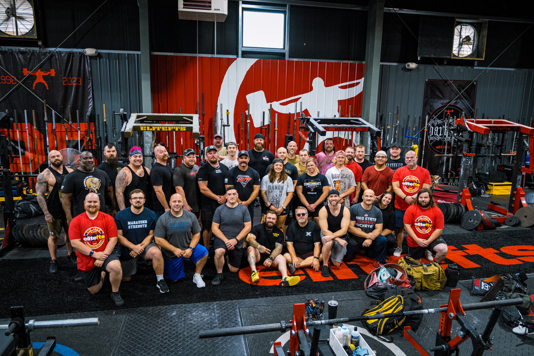 Group of people posing for a photo in a gym setting with various equipment and branding.