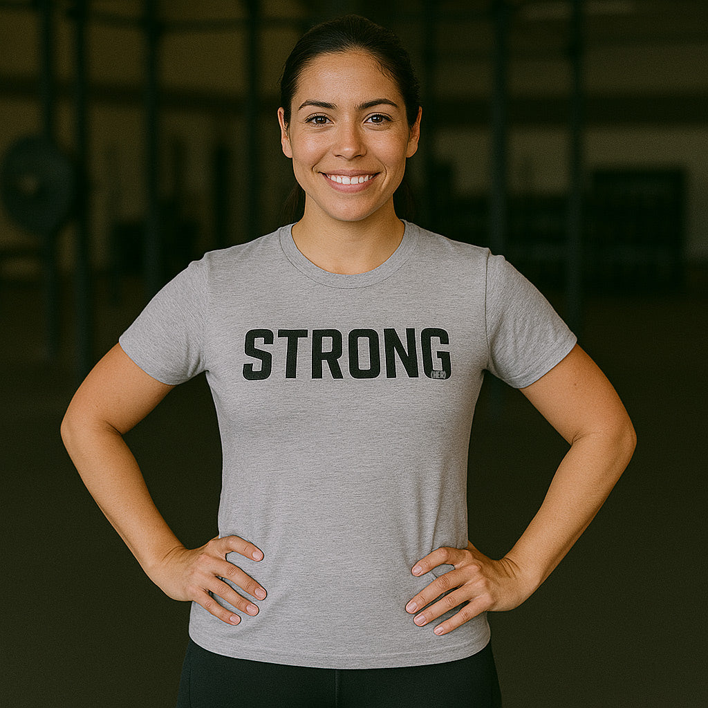 Woman wearing a gray t-shirt with 'STRONG' printed on it, standing in a gym setting-all-groups