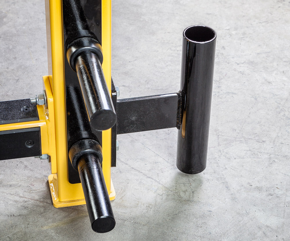 Black metal pipe being cut by a yellow hydraulic cutter on a concrete floor.