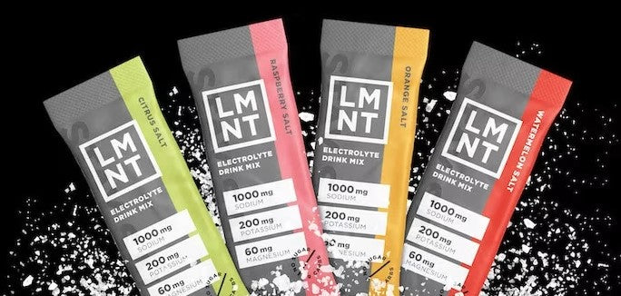 Five packets of LMNT electrolyte drink mix on a black background with white powder.