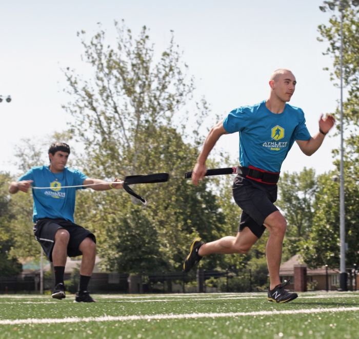 Two athletes in blue shirts playing a game on a sports field with trees in the background