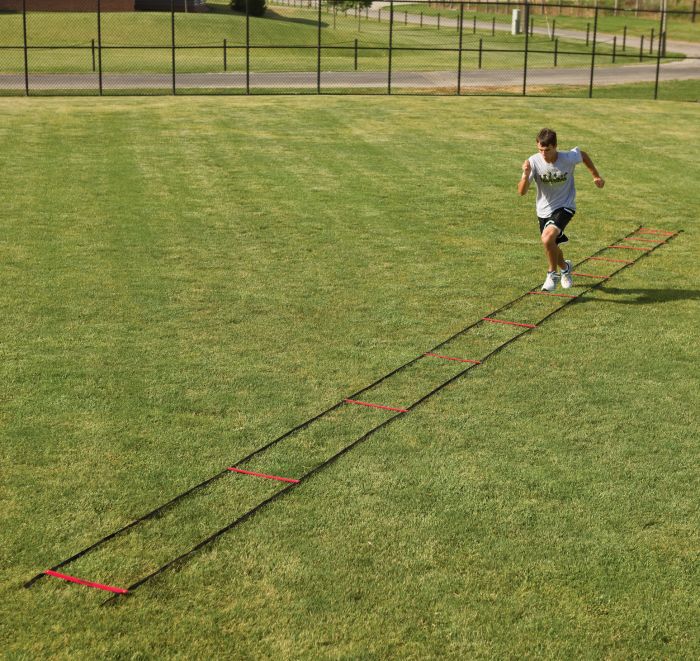 Person running on a grassy field with a long ladder training tool.
