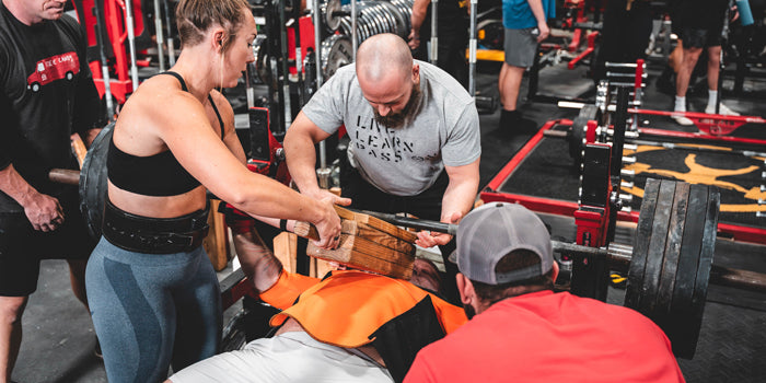 coach behind lifter as he squatsguy squatting with guys watching is every move