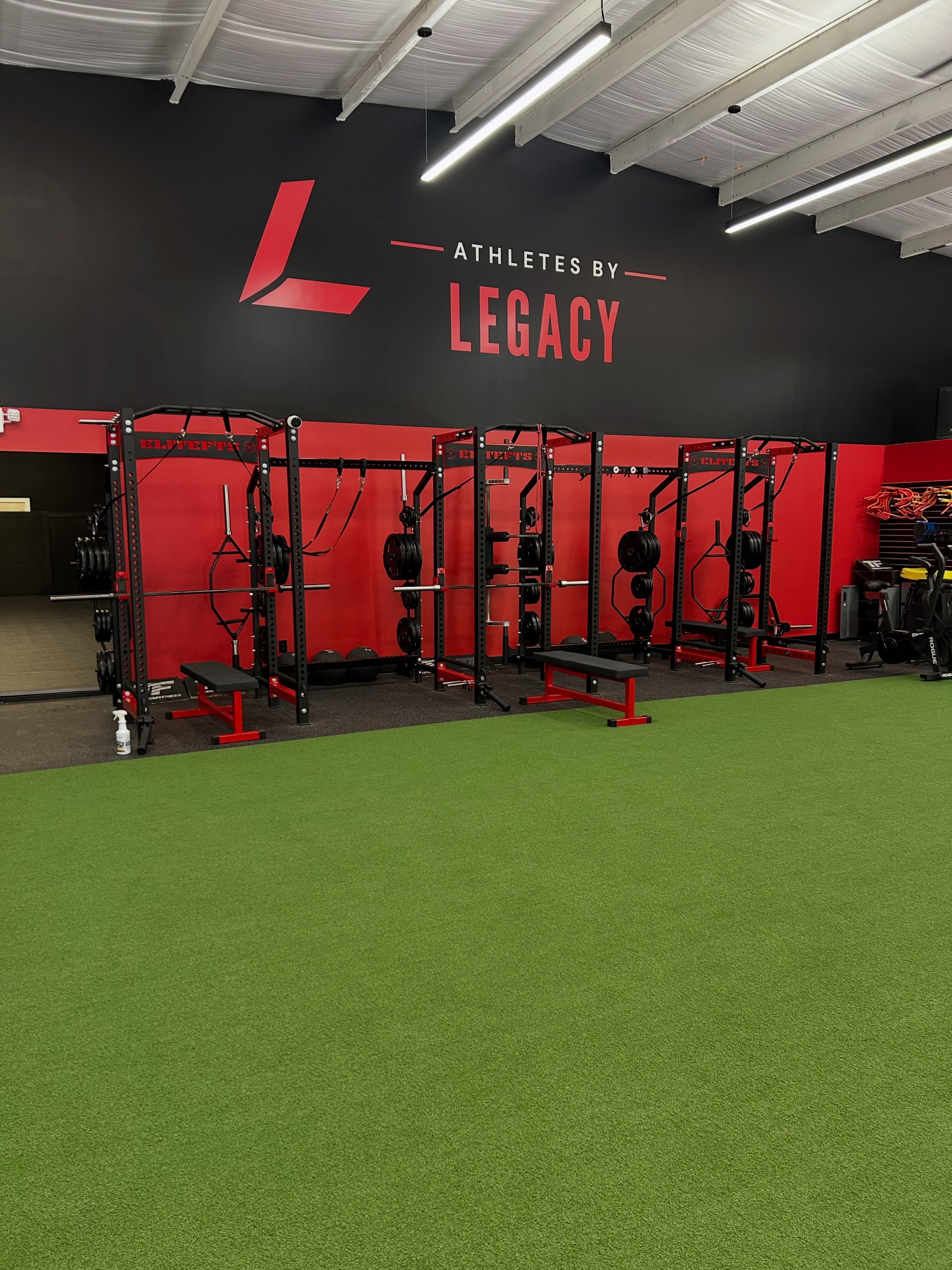 Red and black training racks beside green turf at Athletes By Legacy in Franklin, Tennessee