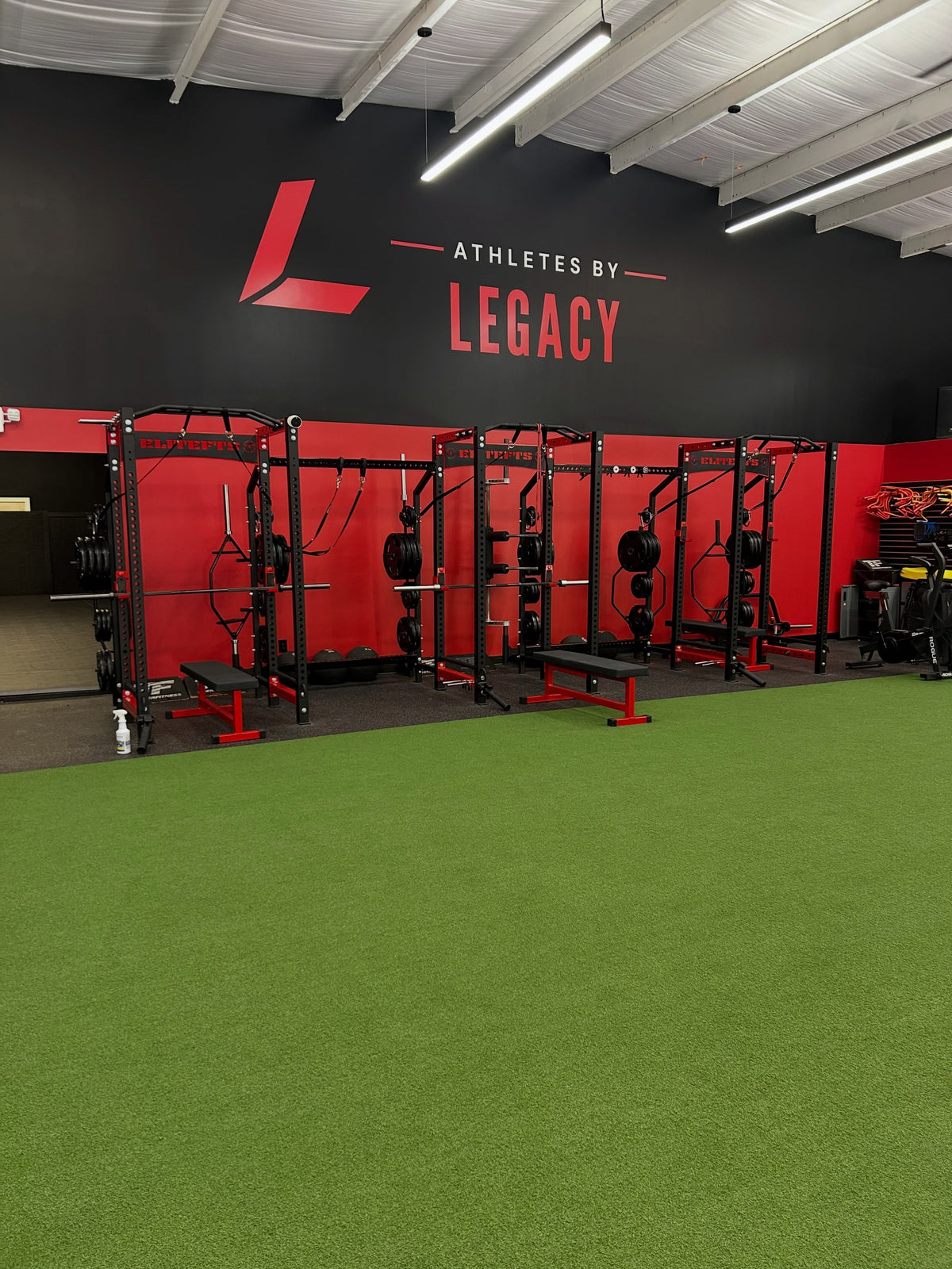 Red and black training racks beside green turf at Athletes By Legacy in Franklin, Tennessee