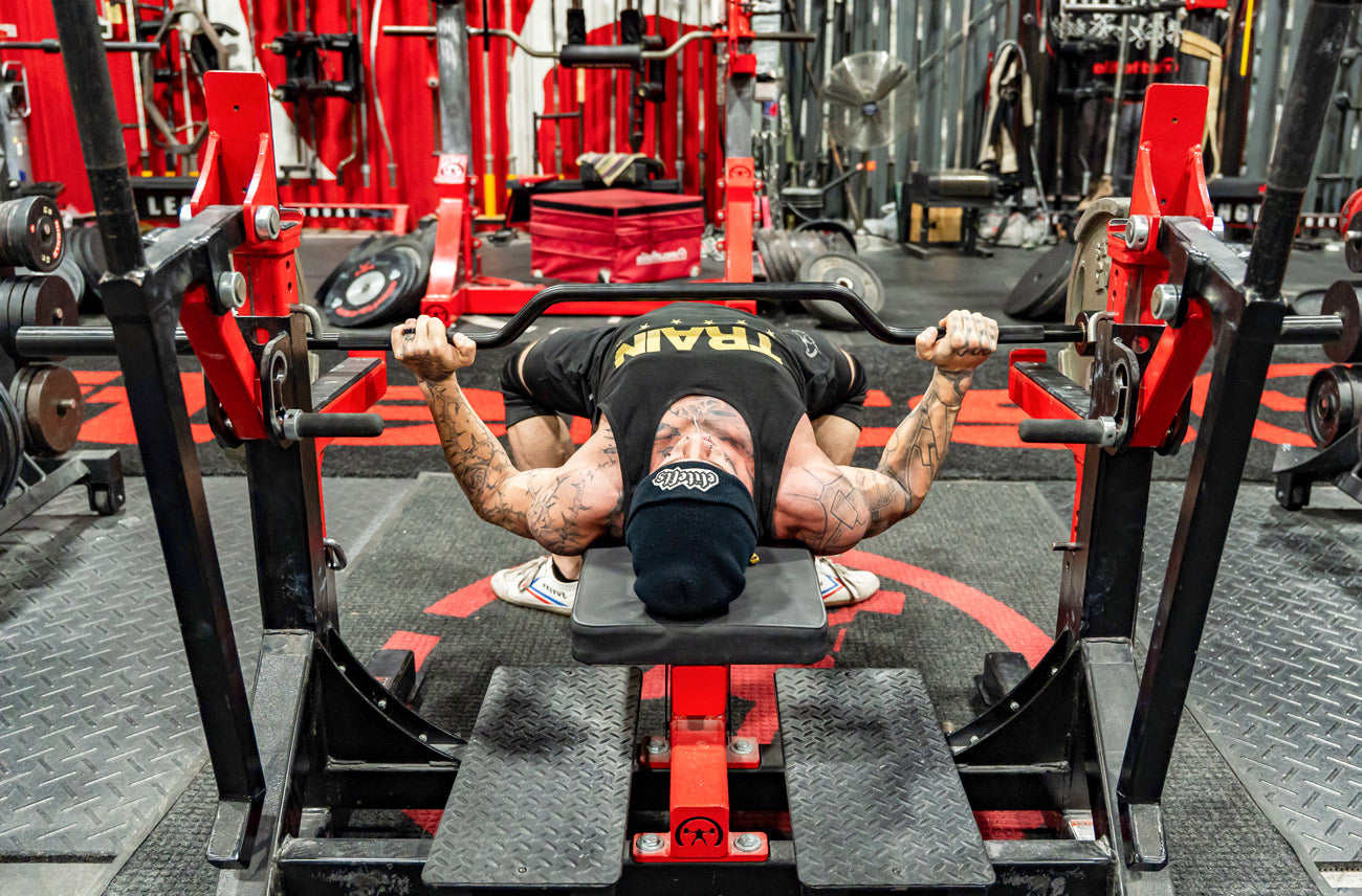 Person performing bench press in a gym setting with red and black equipment.