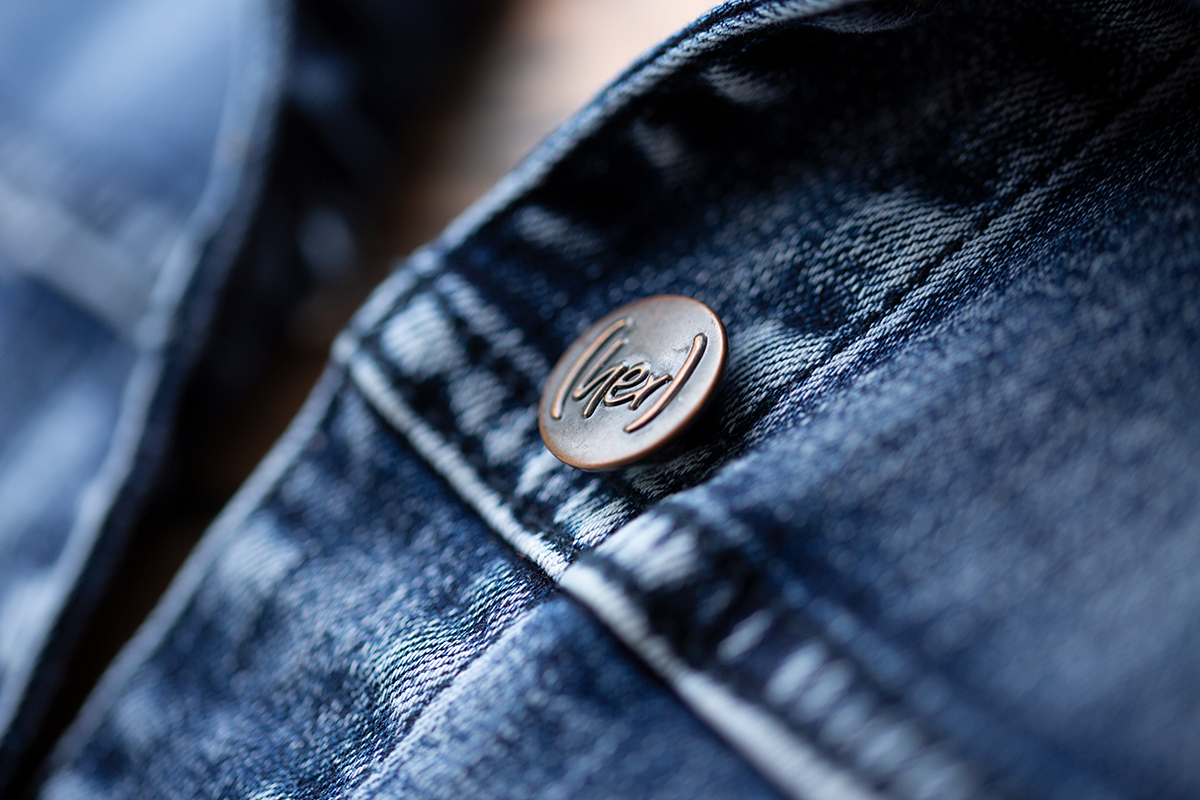 Close-up of a blue denim jacket with a button featuring a logo.