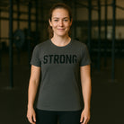 Woman wearing a dark gray t-shirt with 'STRONG' printed on it in a gym setting-all-groups