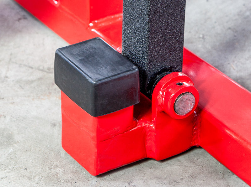 Close-up of a red metal jack with black rubber feet on a concrete floor.