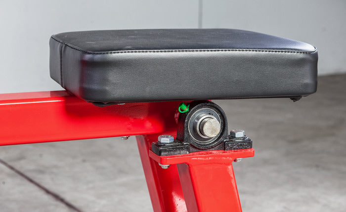 Close-up of a red mechanical component with a black cushioned seat on a gray background