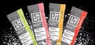 Five packets of LMNT electrolyte drink mix on a black background with white powder.