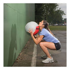 Person playing with a medicine ball against a green wall outdoors
