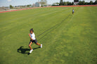 Two people running on a grassy field with a long object, possibly a rope or cable.