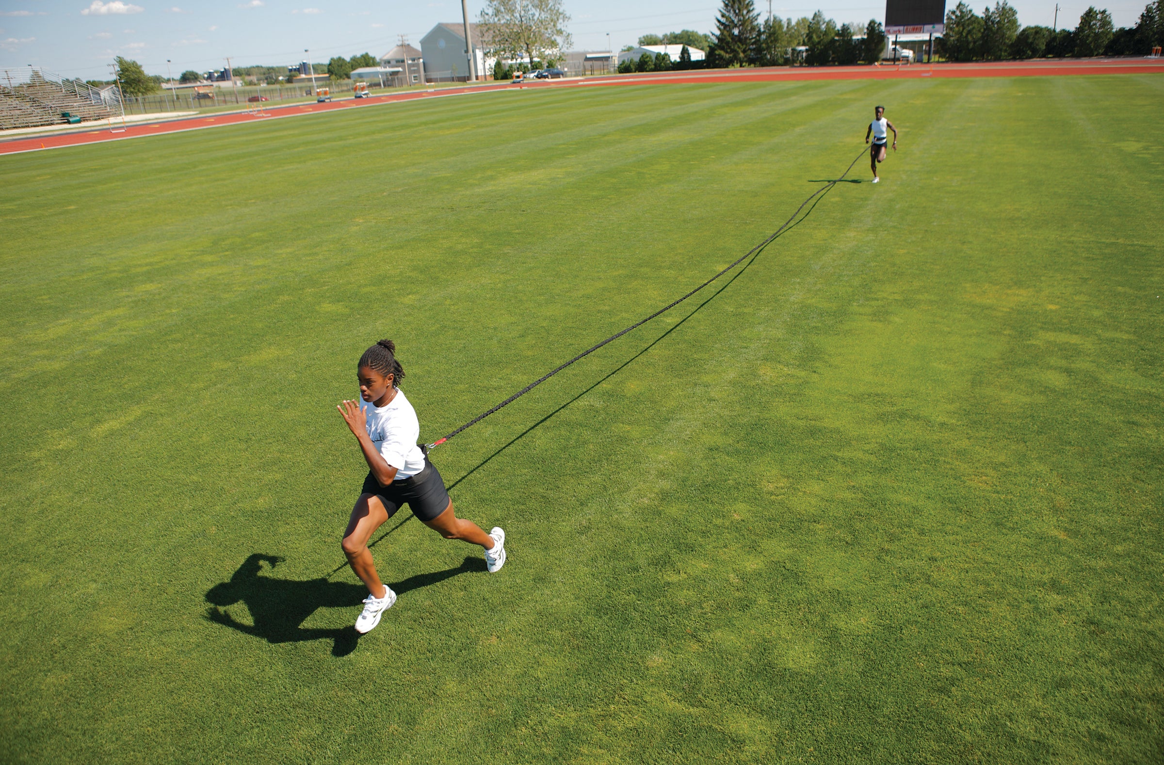 Two people running on a grassy field with a long object, possibly a rope or cable.