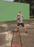 Man running through a red agility ladder on a basketball court with a green wall in the background.