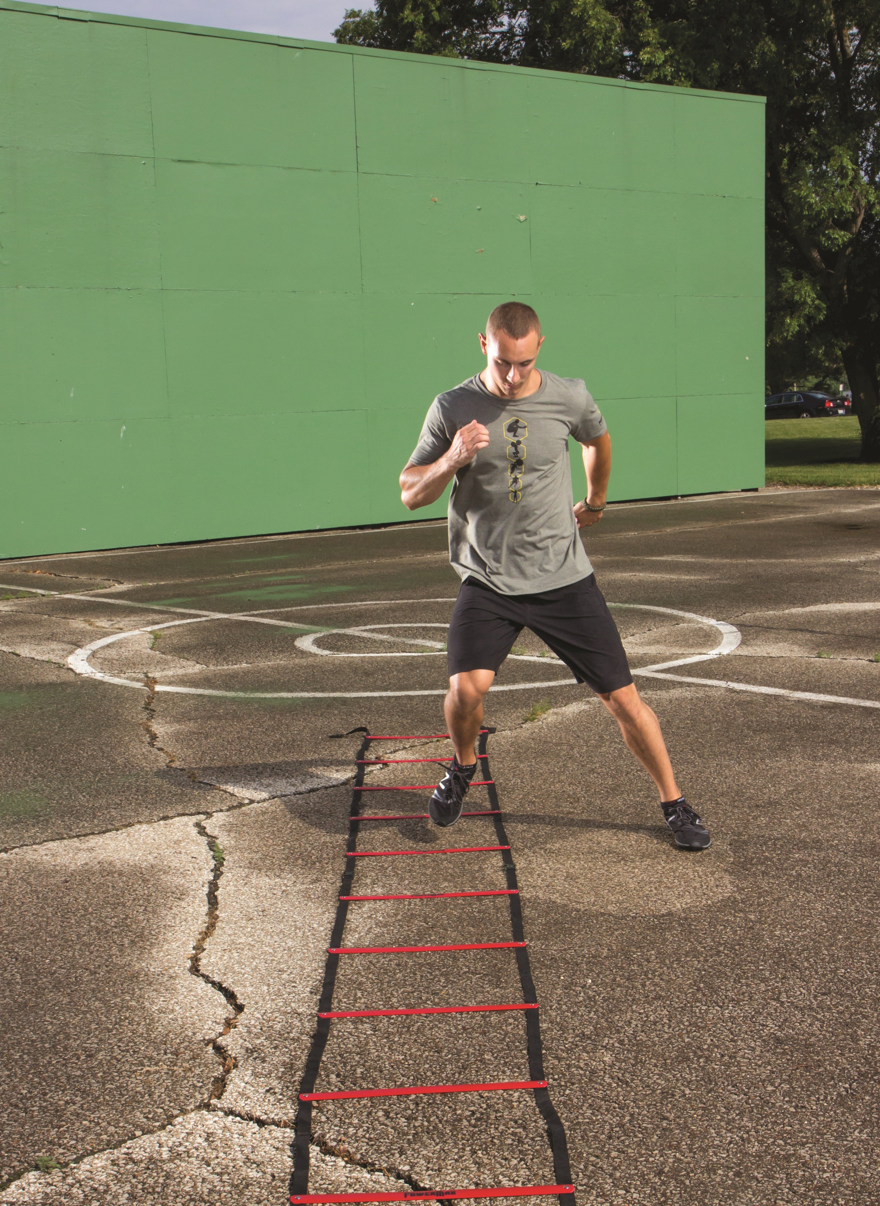 Man running through a red agility ladder on a basketball court with a green wall in the background.